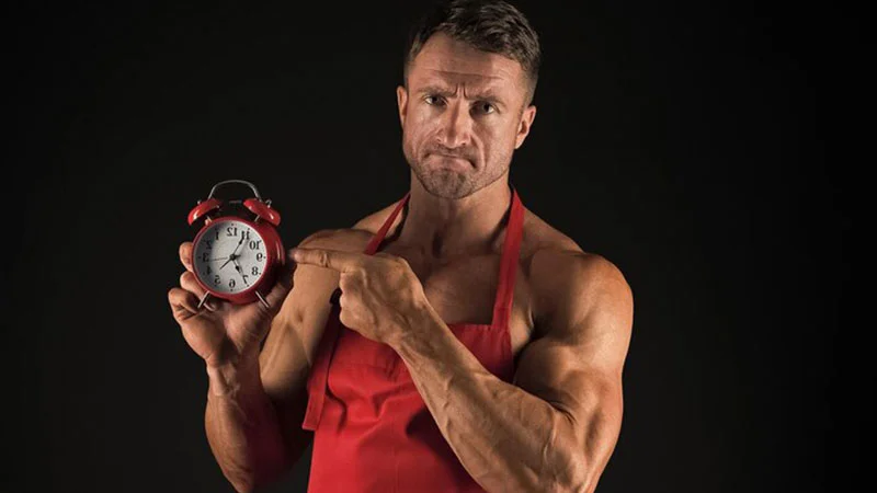 ورزشکار مرد در حال اشاره به ساعت برای نشان دادن اهمیت تمپو در بدنسازی